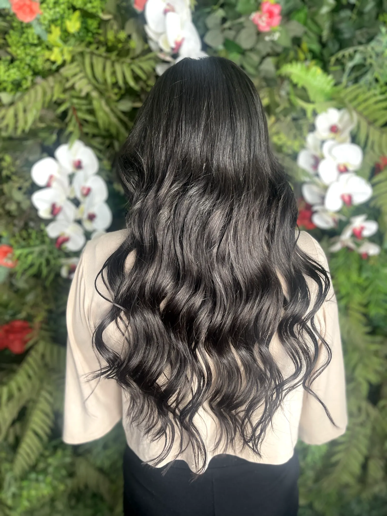Mega hair preto ondulado comprido fundo floral — resultado extensão capilar Scarlett Caroline Beauty